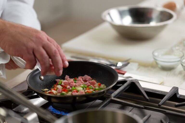 Chef adding diced ham to a skillet with diced peppers and onions.