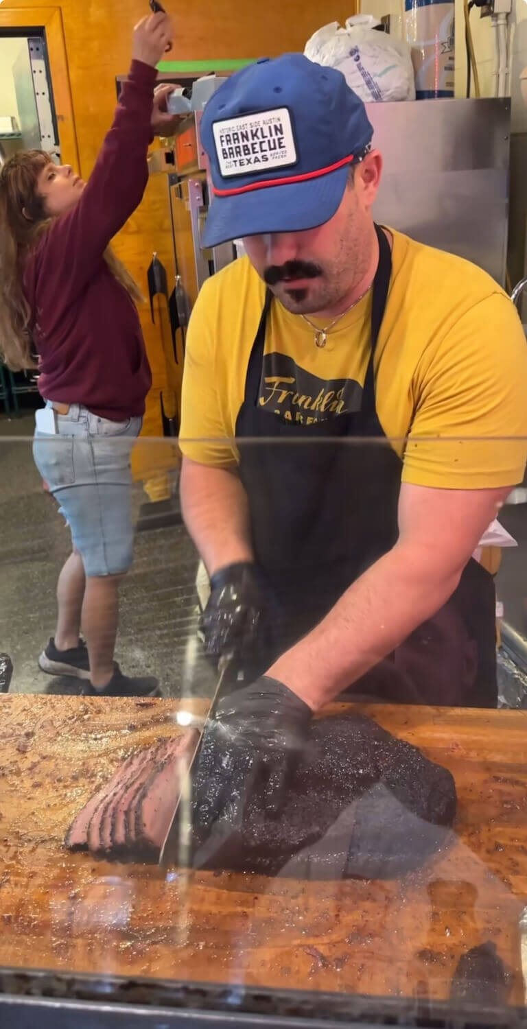 Michael Fields slices perfectly even cuts of brisket on a wood cutting board.