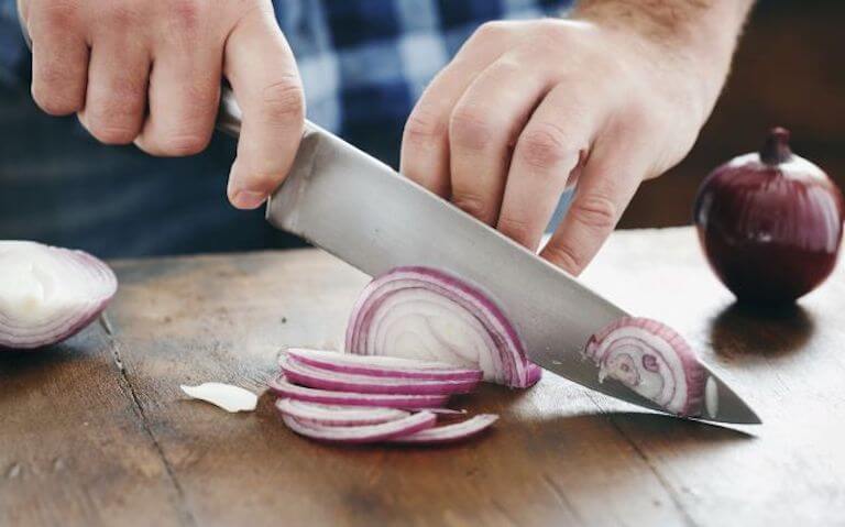 Person using a knife to cut onions on a cutting board