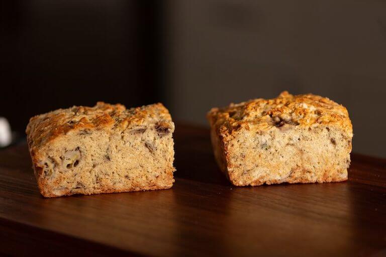 A cross-section of a fresh banana bread loaf on a wooden surface. 