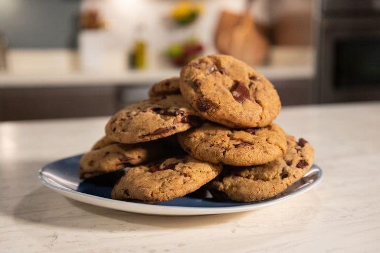 A pile of chocolate chip cookies on a blue plate in a kitchen.