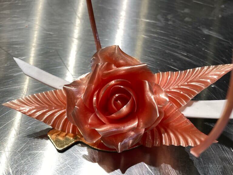 A pink sugar rose stretched on a stainless steel work surface.