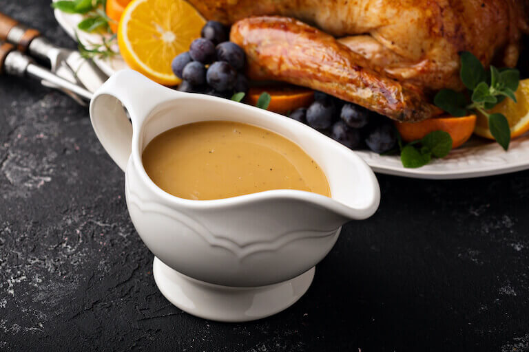 A gravy boat full of smooth gravy sits next to a roasted turkey.