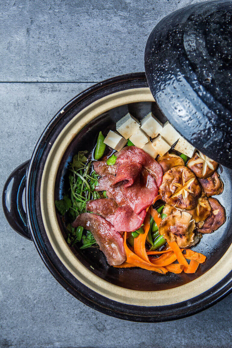 A hot bowl of shabu-shabu beef with several vegetables seen from directly above.