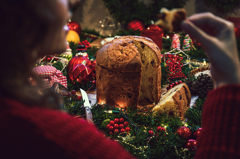 A panetone sits in the center of a wrath surrounded by Christmas decorations.