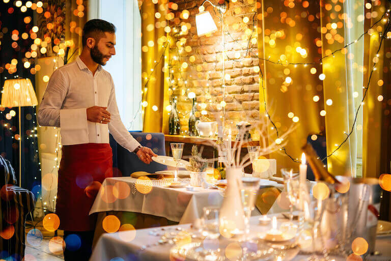 A waiter sets a table in a holiday-light decorated restaurant.