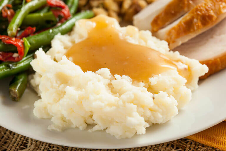 Mashed potatoes sit at the front of a plate also containing turkey and string beans.