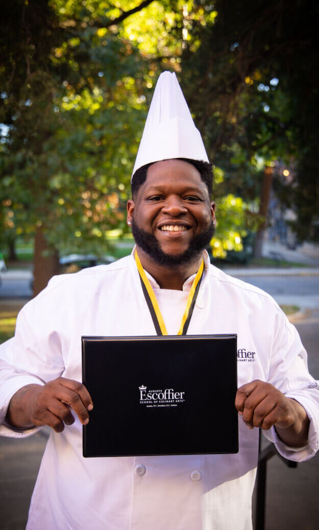 Escoffier Boulder campus culinary graduate smiles proudly while holding his diploma