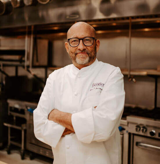 Kirk Bachmann smiling while standing in the professional classroom kitchen at the Escoffier Boulder, Colorado campus with his arms crossed