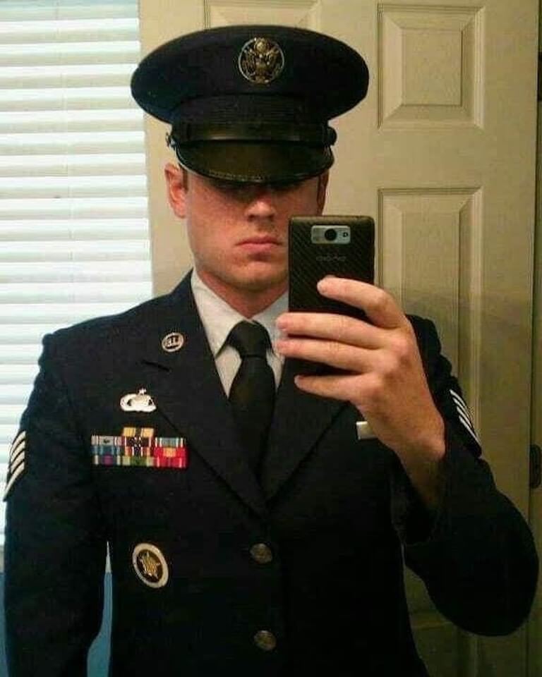 Mason Snyder is taking a selfie while wearing a neatly pressed Air Force uniform and standing in front of a white door.